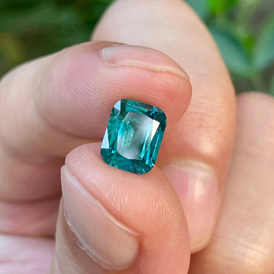 Hand holding a blue gemstone with a blurred green background